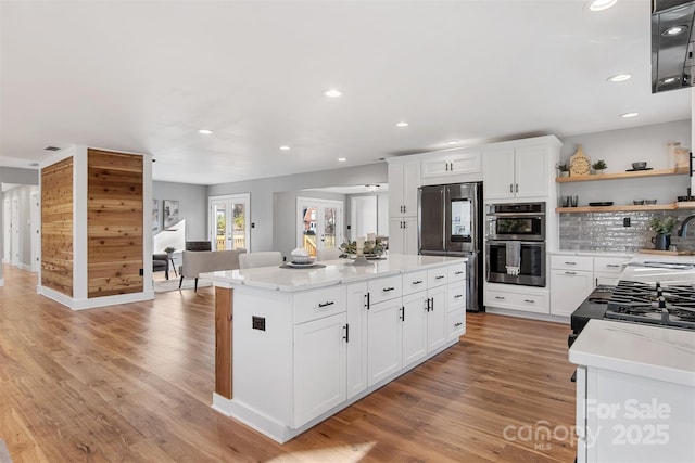 kitchen featuring a center island, appliances with stainless steel finishes, light wood-style floors, white cabinets, and open shelves