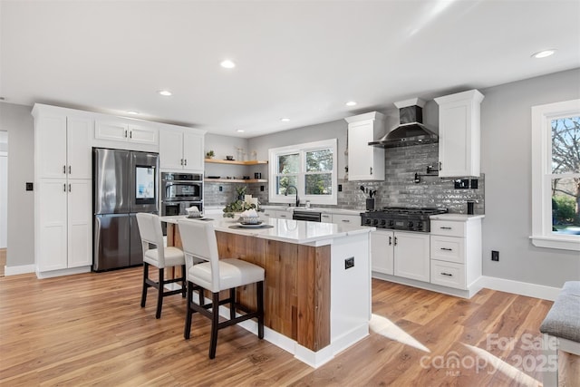 kitchen featuring white cabinetry, stainless steel appliances, light countertops, and wall chimney range hood