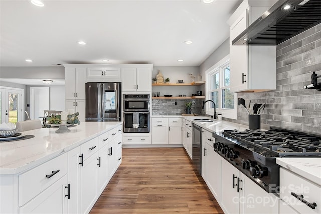 kitchen with light stone counters, stainless steel appliances, wall chimney exhaust hood, and light wood-style flooring