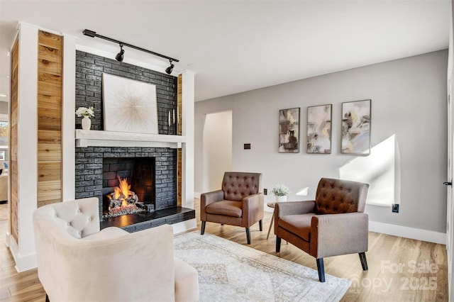 living area with a brick fireplace, rail lighting, wood finished floors, and baseboards