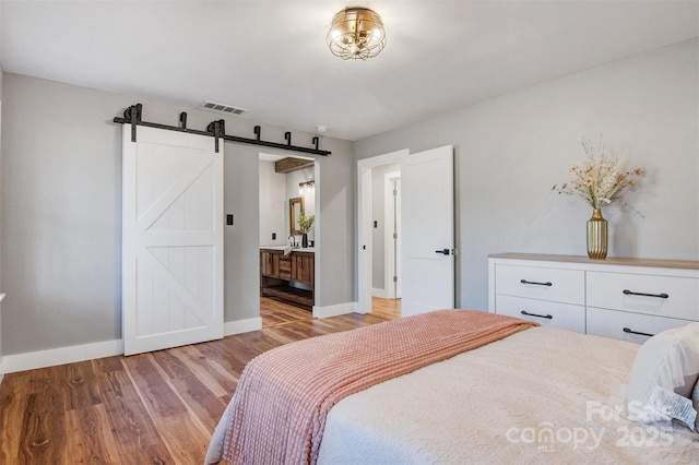 bedroom featuring a barn door, baseboards, visible vents, and light wood finished floors