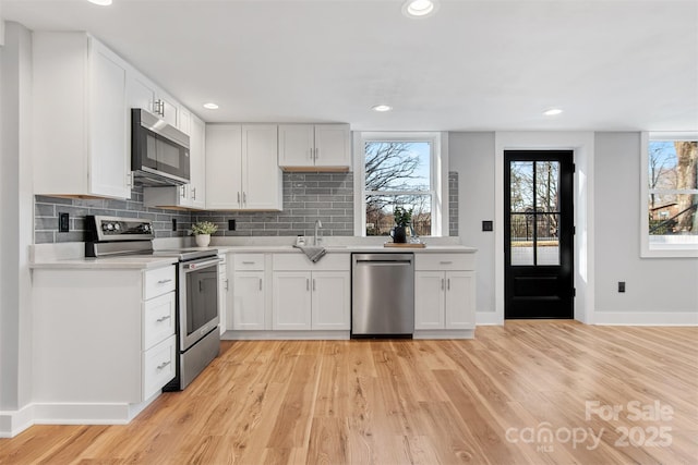 kitchen featuring light countertops, light wood-style floors, tasteful backsplash, and appliances with stainless steel finishes