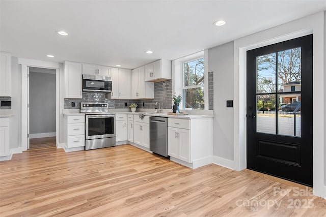 kitchen featuring stainless steel appliances, light wood finished floors, decorative backsplash, and light countertops