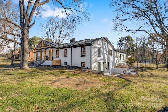 rear view of property with a standing seam roof, fence, a yard, metal roof, and a chimney