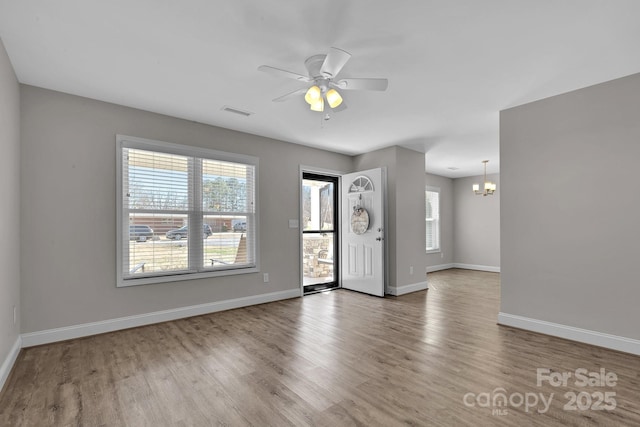 interior space with ceiling fan with notable chandelier, wood finished floors, baseboards, and a wealth of natural light