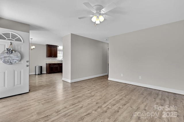 unfurnished living room featuring ceiling fan with notable chandelier, baseboards, light wood finished floors, and a sink