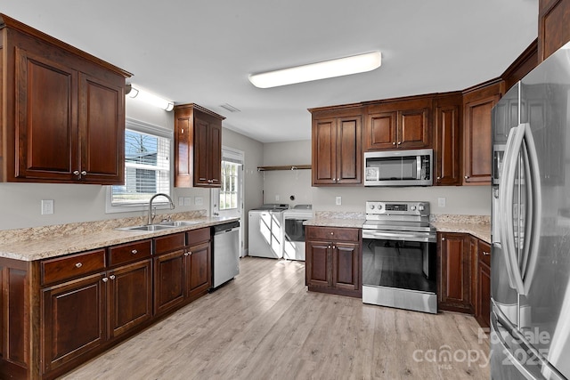 kitchen with light countertops, light wood-style floors, washer and dryer, stainless steel appliances, and a sink