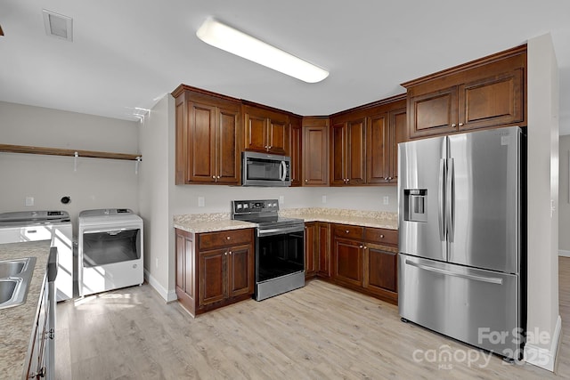 kitchen with visible vents, independent washer and dryer, a sink, light wood-style floors, and appliances with stainless steel finishes