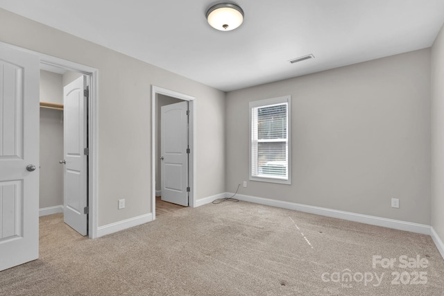 unfurnished bedroom with visible vents, a walk in closet, baseboards, carpet floors, and a closet