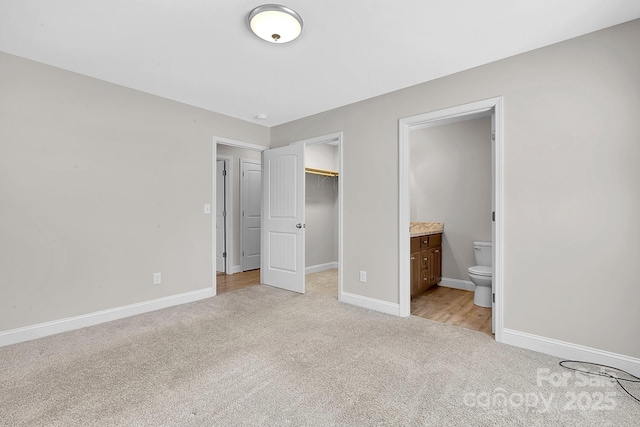 unfurnished bedroom with a spacious closet, light colored carpet, ensuite bath, and baseboards