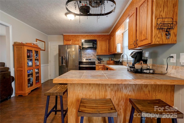 kitchen featuring crown molding, tile countertops, a kitchen bar, appliances with stainless steel finishes, and a sink