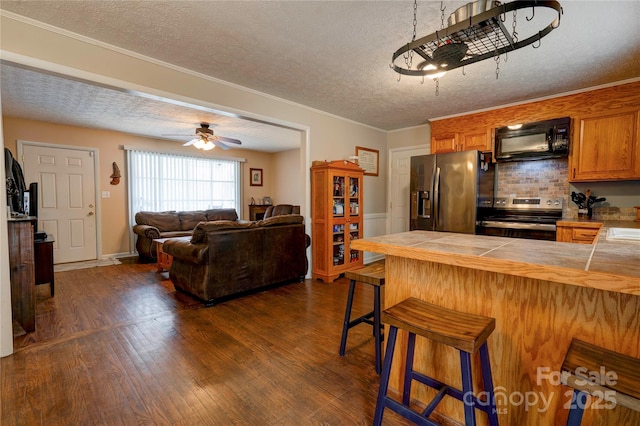 kitchen with tile countertops, brown cabinets, appliances with stainless steel finishes, a kitchen breakfast bar, and dark wood-style flooring