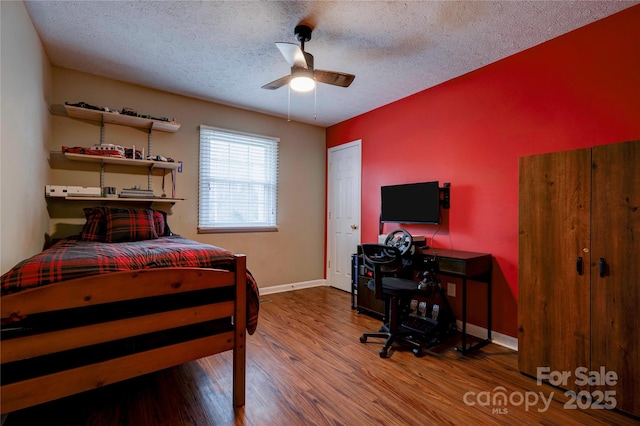 bedroom with ceiling fan, a textured ceiling, baseboards, and wood finished floors