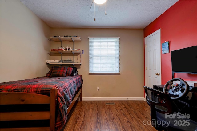 bedroom with a ceiling fan, wood finished floors, baseboards, and a textured ceiling