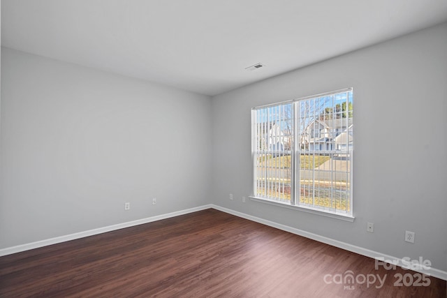 empty room with dark wood-style floors, baseboards, visible vents, and a wealth of natural light