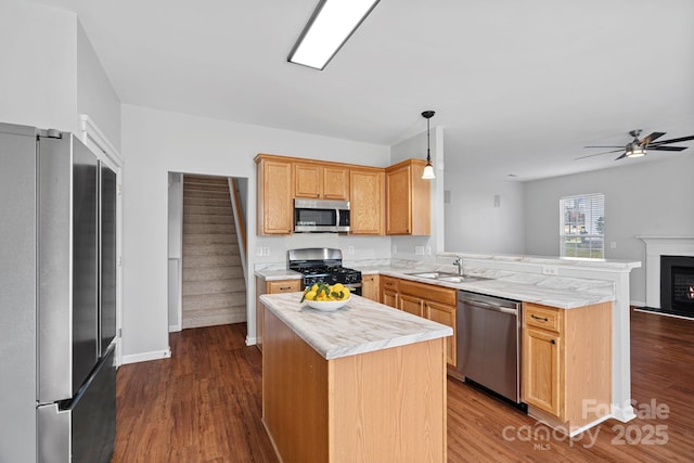 kitchen featuring a peninsula, a sink, light countertops, appliances with stainless steel finishes, and dark wood-style floors