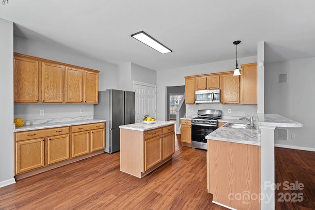 kitchen with a peninsula, a sink, a kitchen island, wood finished floors, and appliances with stainless steel finishes