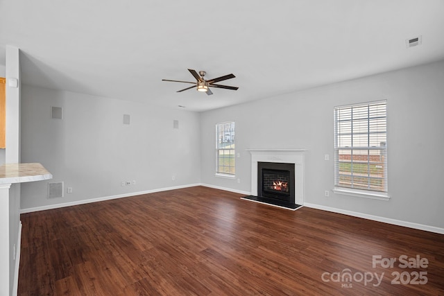 unfurnished living room featuring a warm lit fireplace, visible vents, and dark wood-type flooring