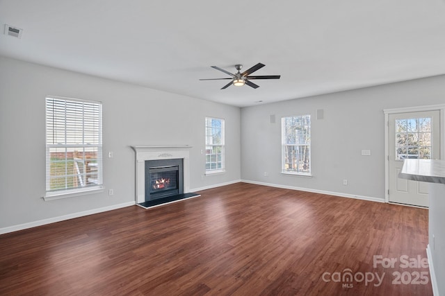 unfurnished living room featuring dark wood-type flooring, a glass covered fireplace, and a wealth of natural light