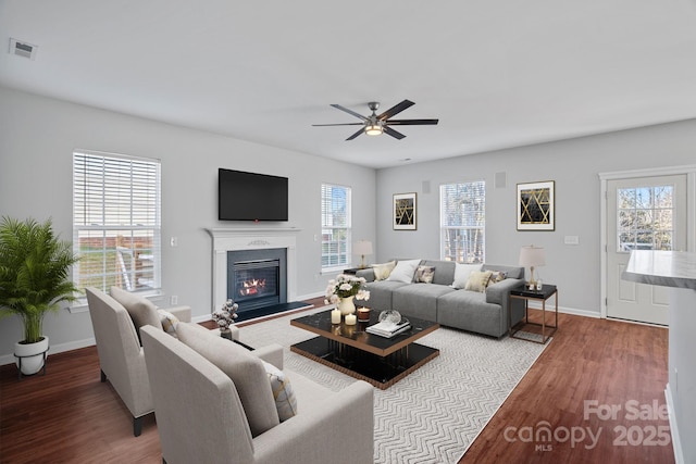 living area featuring a glass covered fireplace, plenty of natural light, wood finished floors, and visible vents