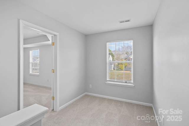 empty room featuring light carpet, visible vents, and baseboards