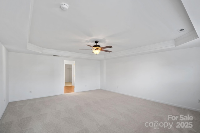 empty room featuring ornamental molding, visible vents, a raised ceiling, and light colored carpet