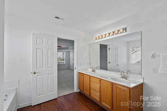 full bathroom with a garden tub, double vanity, visible vents, a sink, and wood finished floors