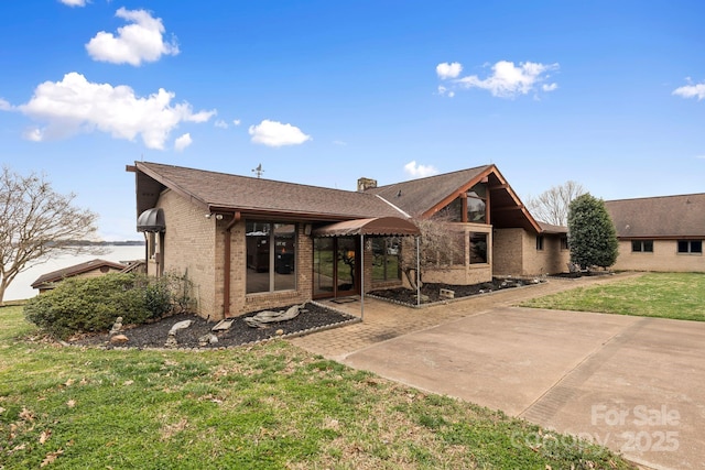 view of front of property with a patio, a front lawn, brick siding, and a chimney