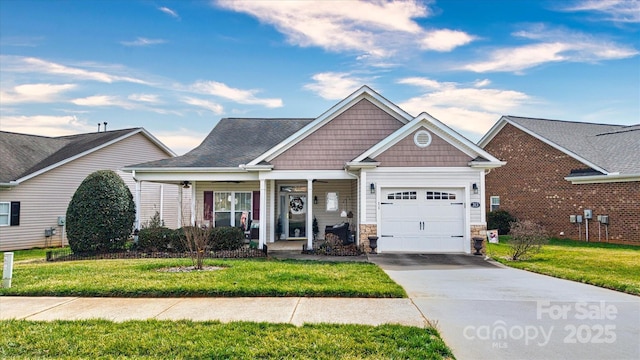 view of front of property with driveway, stone siding, a porch, an attached garage, and a front yard