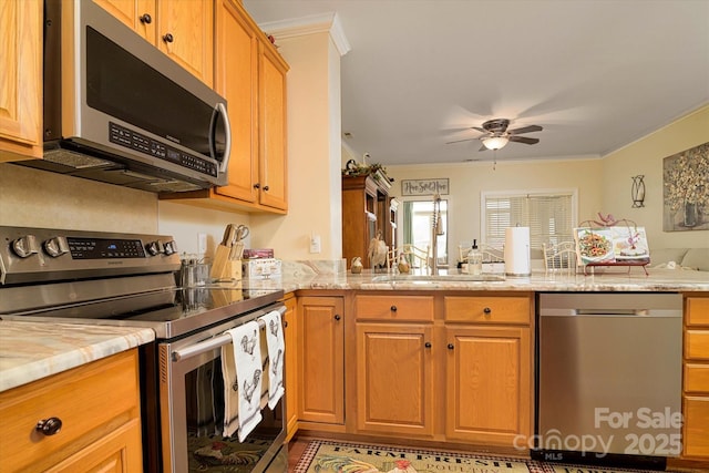 kitchen featuring ceiling fan, light stone countertops, ornamental molding, appliances with stainless steel finishes, and a sink