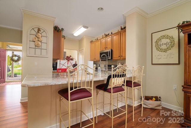 kitchen featuring stainless steel microwave, a peninsula, wood finished floors, and ornamental molding