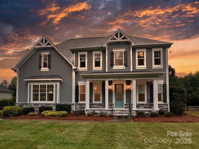 view of front facade with covered porch, a shingled roof, and a front yard