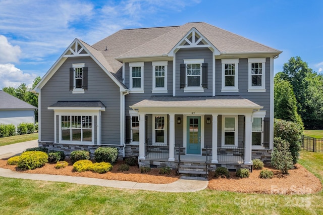 craftsman-style home featuring covered porch, stone siding, a shingled roof, and a front lawn