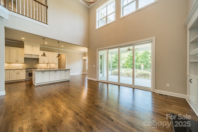 unfurnished living room with baseboards, visible vents, dark wood finished floors, crown molding, and a sink