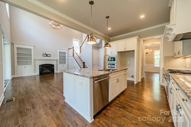 kitchen with stainless steel appliances, a sink, ornamental molding, dark wood-style floors, and a glass covered fireplace