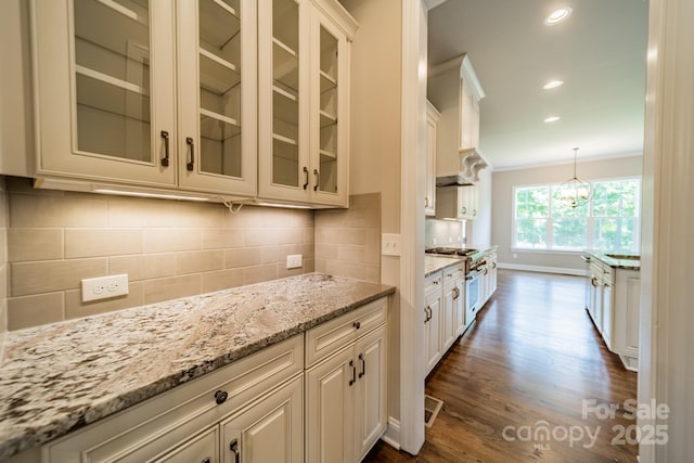 kitchen featuring light stone counters, ornamental molding, dark wood-type flooring, backsplash, and gas stove