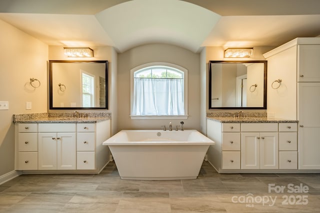 bathroom with lofted ceiling, two vanities, a soaking tub, and a sink