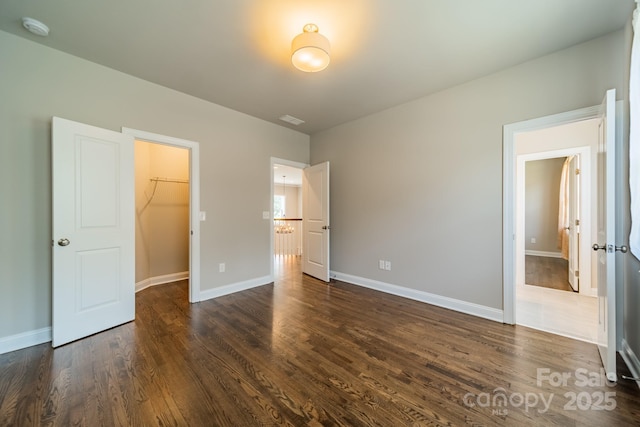 unfurnished bedroom featuring visible vents, baseboards, dark wood-type flooring, a walk in closet, and a closet