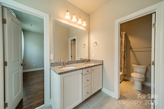 full bathroom with baseboards, a sink, toilet, and double vanity