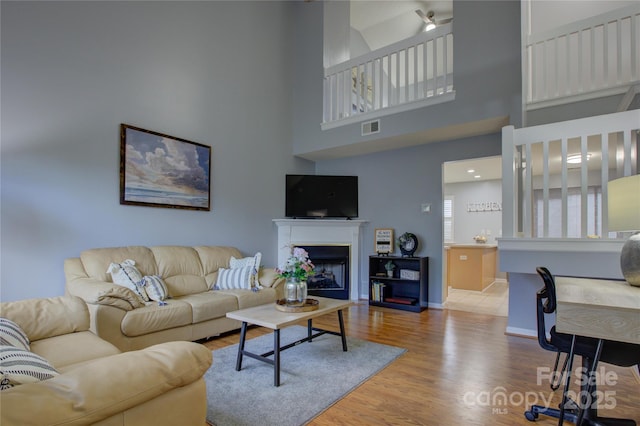 living room with a fireplace, visible vents, a towering ceiling, wood finished floors, and baseboards