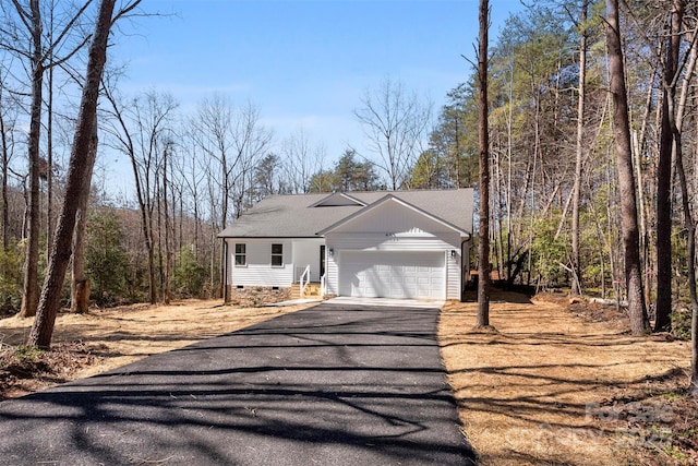 view of front of property with aphalt driveway, roof with shingles, crawl space, a view of trees, and a garage