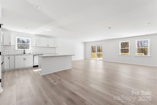 kitchen with a kitchen island, a sink, decorative backsplash, dishwasher, and light wood finished floors