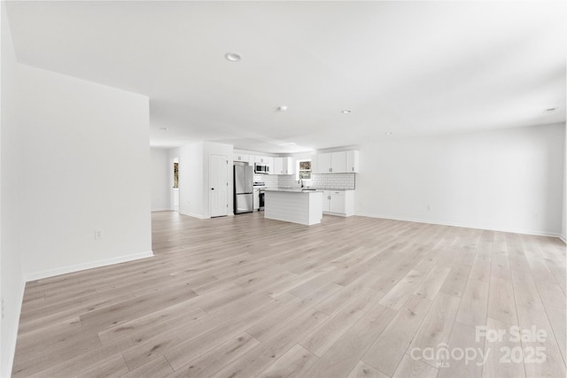 unfurnished living room with light wood-style flooring, baseboards, a sink, and recessed lighting