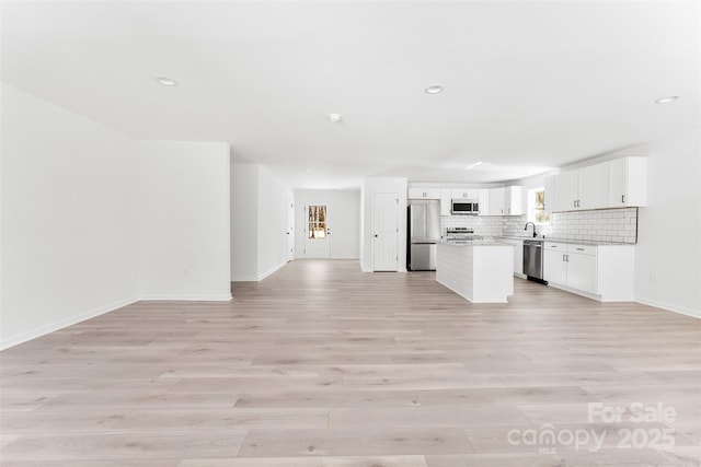 unfurnished living room with light wood-type flooring, baseboards, a sink, and recessed lighting