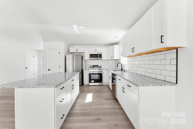 kitchen featuring a sink, a center island, light wood-style floors, appliances with stainless steel finishes, and decorative backsplash