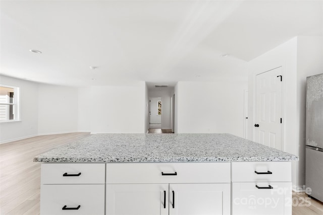 kitchen with light stone counters, freestanding refrigerator, open floor plan, and light wood-style flooring