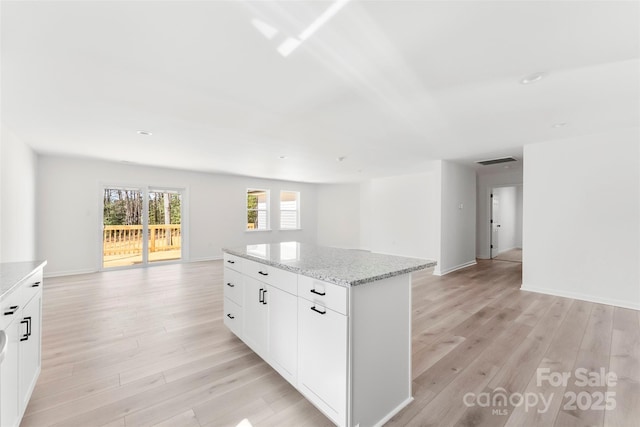 kitchen featuring a center island, visible vents, open floor plan, light wood-type flooring, and light stone countertops