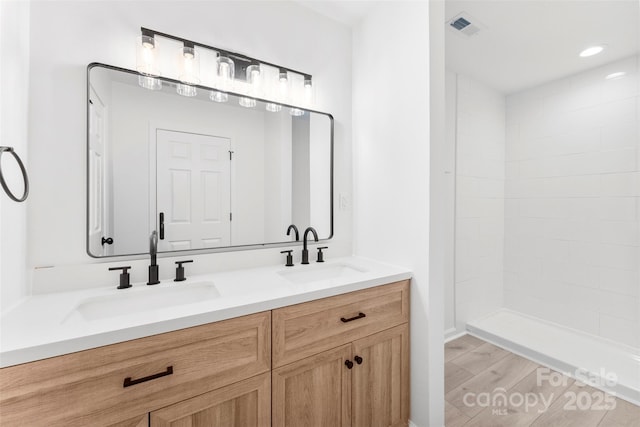 full bath featuring double vanity, wood finished floors, a sink, and visible vents