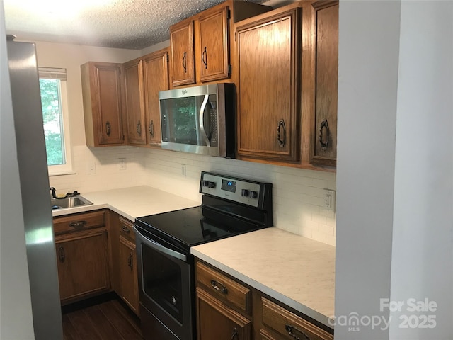 kitchen with a textured ceiling, light countertops, appliances with stainless steel finishes, backsplash, and dark wood-style floors