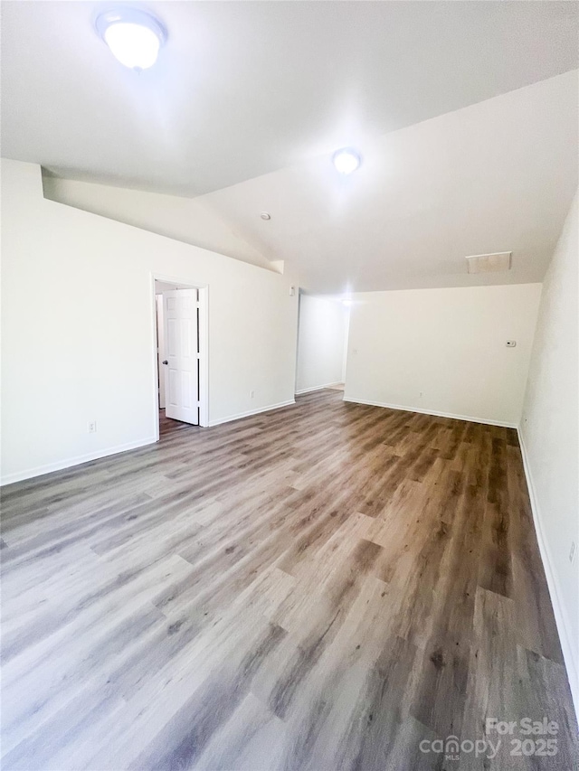 empty room featuring baseboards, vaulted ceiling, and wood finished floors
